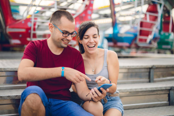 istock Young couple using phone in amusement park 1091841462