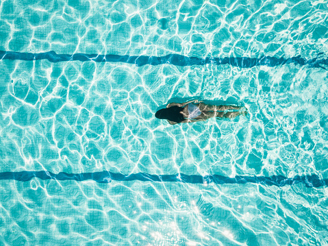 Drone view on teenage girl diving in blue swimming pool