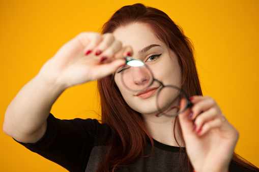 Studio portrait of a 16 year old teen girl holding glasses on a yellow background