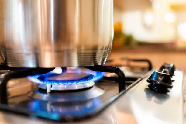 Photo of Macro closeup of modern luxury gas stove top with blue fire flame knobs and stainless steel pot with reflection and bokeh blurry blurred background