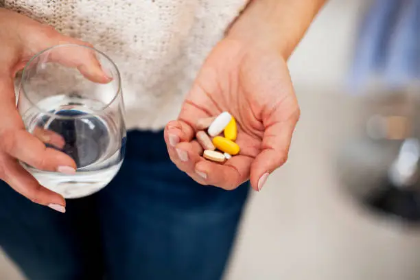 unrecognizable woman holding vitamins in one hand and water in the other