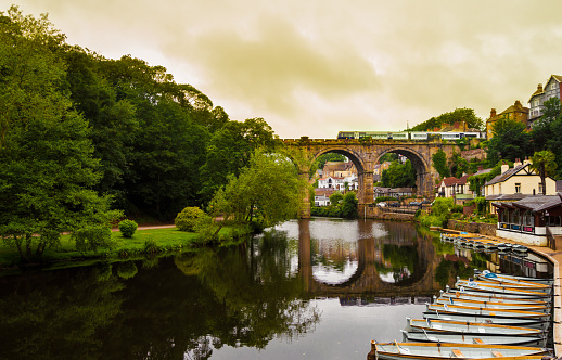View of the Nidd River and rowing boats from the ruins of Knaresborough Castle with the train passing through the old bridge in a cloudy day.