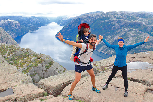 A cheerful couple and their little kid in the summit of the Pulpit Rock (Preikestolen), one of the world's most spectacular viewing points. A plateau that rises 604 meters above the Lysefjord, Norway.