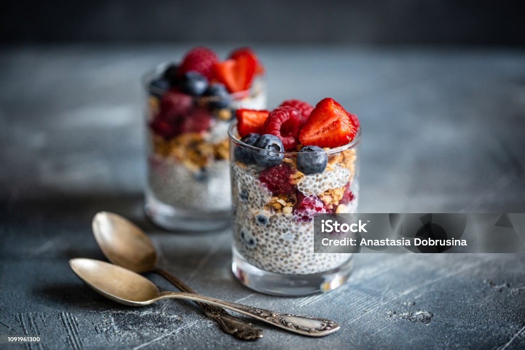 Healthy dessert with chia seeds, blueberries, strawberries, raspberries and granola. Horizontal. Healthy vanilla chia pudding in glass with fresh berries on vintage concrete table. Copy space. Banner. Chia Seed Stock Photo