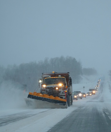 Snow plow clearing snow off highway in January 2019 snow storm with long line of cars following behind