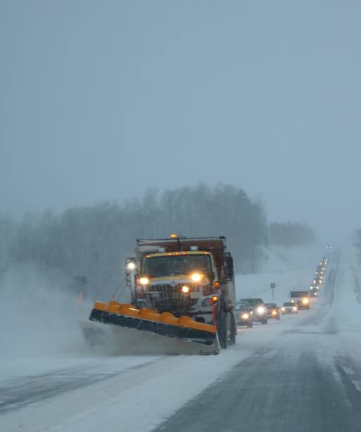 Photo of Snow plow moving drifting snow of road in squalls with trail of cars following