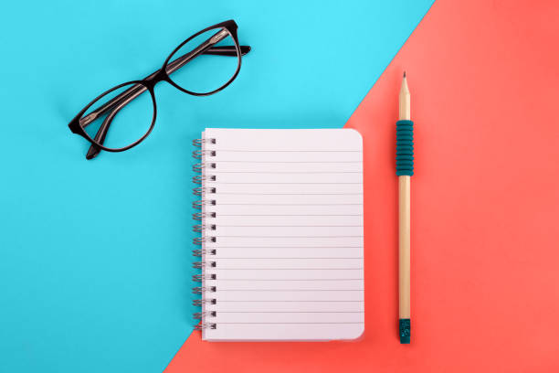 Spiral notepad, pencil and glasses on bright background.