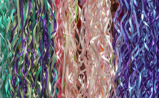 Background of multicolored ribbon streamers hanging vertically including green purple pink white and yellow