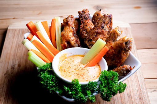 A delicious bowl o Keto hot wings served with a cup of hot sauce, carrot and celery sticks garnished with parsley