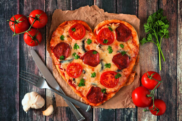 istock Heart shaped pizza for Valentines Day over dark wood, table scene with ingredients 1092007256