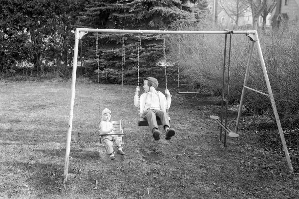 Two little boys playing on back yard swing set in the autumn of 1965. Waterloo, Iowa, USA. Scanned film.