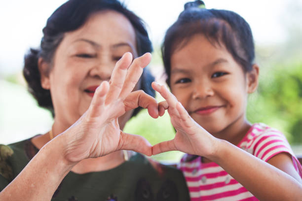 Asian grandmother and little child girl making heart shape with hands together with love stock photo