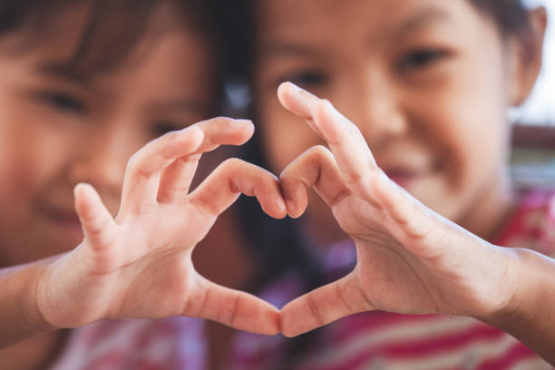 Two cute asian child girls making heart shape with hands together with love stock photo