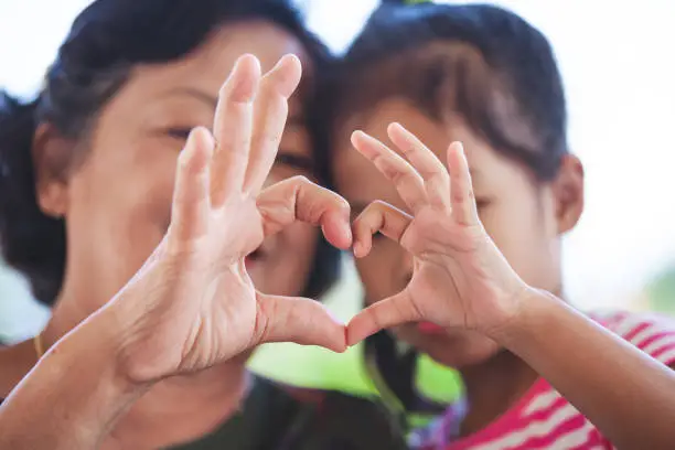 Photo of Asian grandmother and little child girl making heart shape with hands together with love