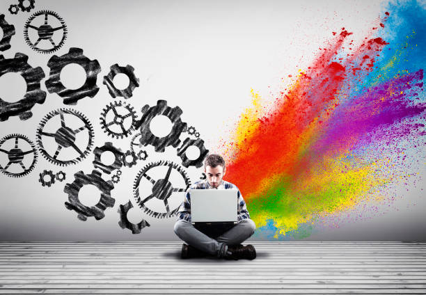 istock Man working on laptop against an wall painted with engine gear wheels and powder explosion. 1092045154
