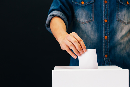 Vista frontal de la persona que voto voto papel en una mesa de votación para elecciones voto en fondo negro photo