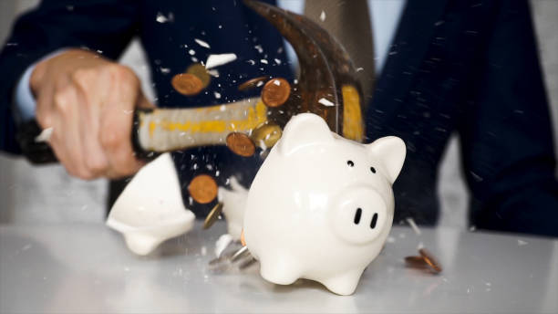 Close-up of businessman using a hammer to smash plenty of coins inside piggybank into pieces as he needs emergency money - using money in financial crisis concept. stock photo