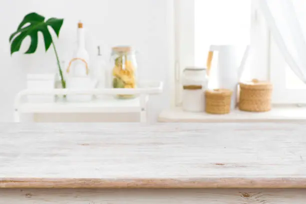 Photo of Wooden table top on blurred kitchen window and shelves background