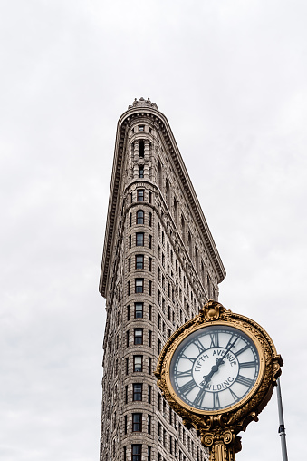 New York City, USA - June 20, 2018: Flatiron Building  in Manhattan. Low angle view against cloudy day with clock on foreground. It is one of the worlds most iconic skyscrapers and a symbol of New York