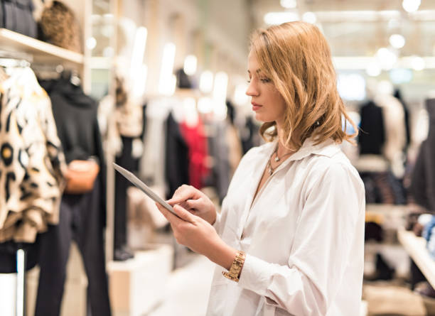 Sales assistant with a digital tablet examining products in a clothing store.