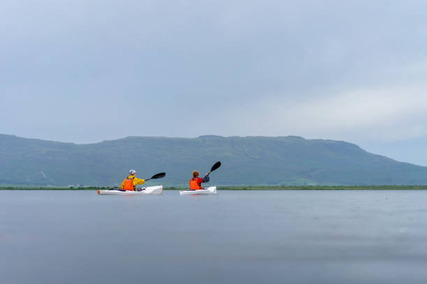 Friends paddling kayak in scenic lake. Male and female are kayaking against cloudy sky. They are enjoying vacation together.