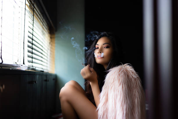portrait charming sexy woman. attractive beautiful women is smoking cigarette or tobacco in living room. gorgeous asian woman feels cold. cigarette is killing her slowly. it"u2019s cause of lung cancer - nicotine healthcare and medicine smoking issues lifestyles imagens e fotografias de stock