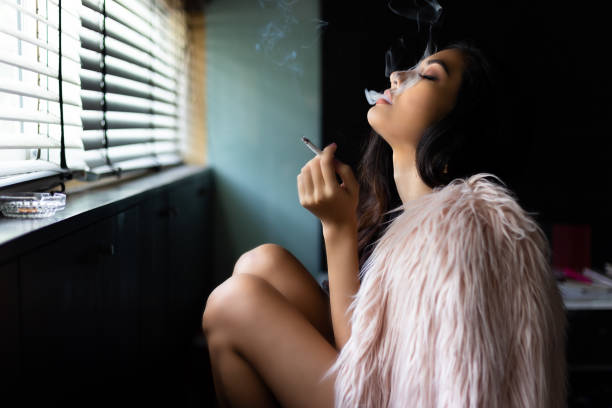 очаровательная красивая сексуальная женщина курит марихуану или сигарету. привлекательная красивая девушка чувствует себя расслабляющей - living room elegance women long hair стоковые фото и изображения