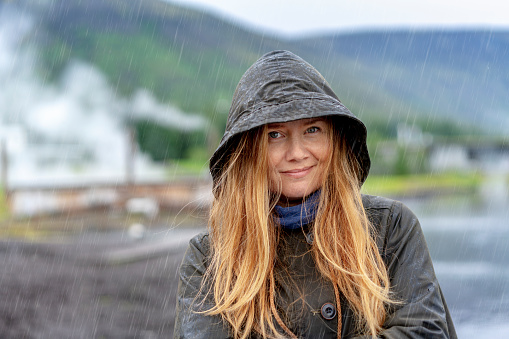 Portrait of beautiful woman wearing raincoat. Smiling female with long hair is standing in rainy season. She is enjoying vacation.