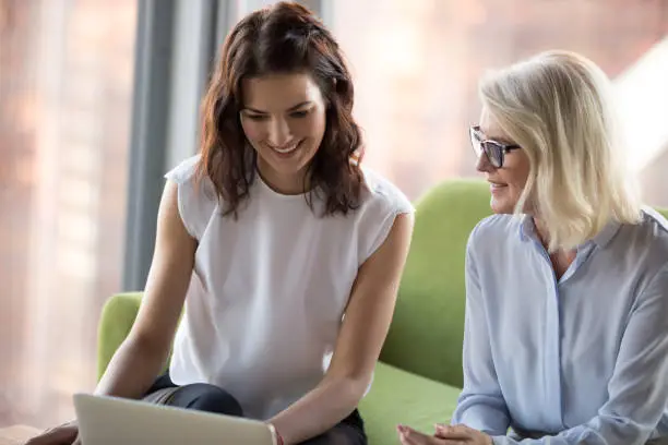 Photo of Senior and young colleagues women sitting looking at laptop screen