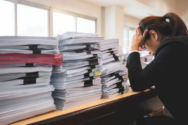 女性会社員は彼女の机の上の書類の多くで困っています。 - paperwork emotional stress women document ストックフォトと画像