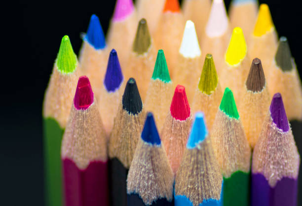 Color image depicting a close up macro view of a collection of colored pencils in a row, on a black background.