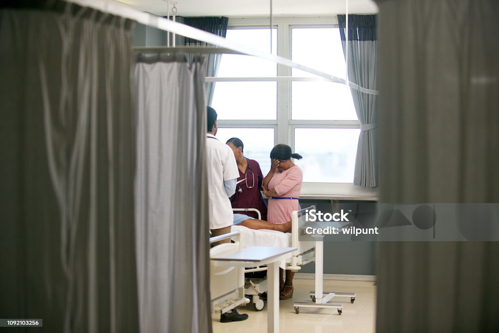 Doctor sharing bad news with family member A male African Doctor sharing bad medical news with a female friend or family member with a nurse supporting her at the patient's bed Cape Town South Africa Death Stock Photo