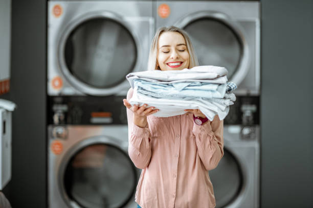 Woman with ironed clothes in the laundry Young woman enjoying clean ironed clothes in the self serviced laundry with dryer machines on the background iron appliance photos stock pictures, royalty-free photos & images