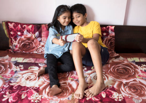 Sibling using mobile phone on bed at home Little brother and sister using mobile phone while relaxing on bed at home indian boy barefoot stock pictures, royalty-free photos & images