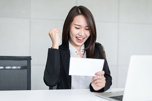 Young beautiful Asian business woman felling happy or success after look at bonus money or salary in an envelop.