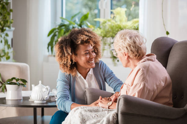 Friendly nurse supporting an eldery lady Female home caregiver talking with senior woman, sitting in living room and listening to her carefully. lounge chair photos stock pictures, royalty-free photos & images