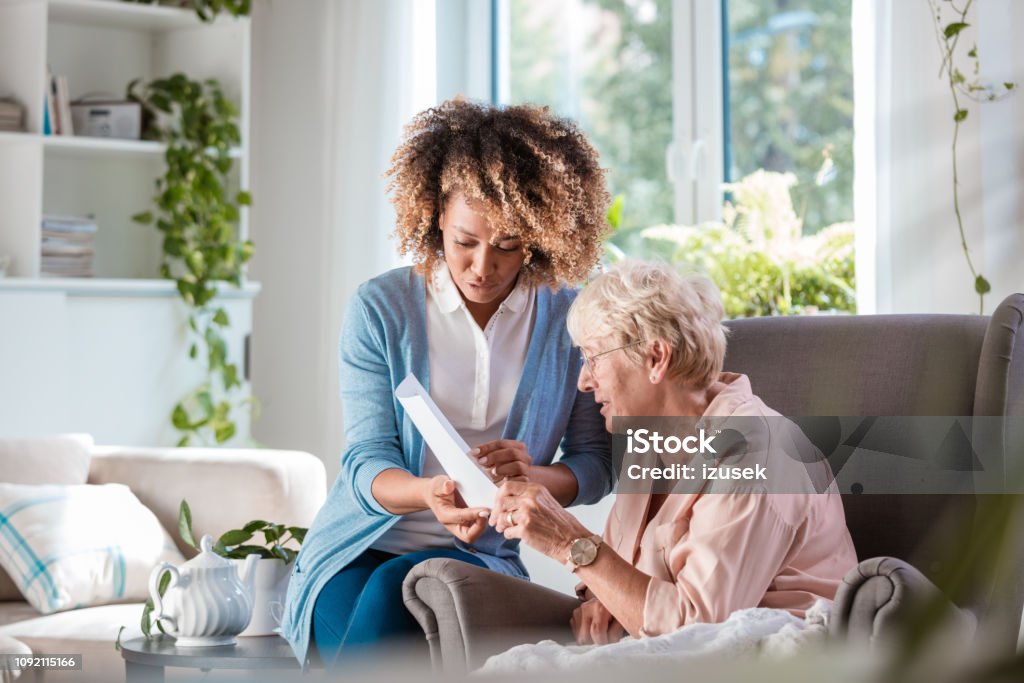 Home nurse taking care of senior woman Female home caregiver supporting senior woman in her house, explaining her documents. Senior Adult Stock Photo