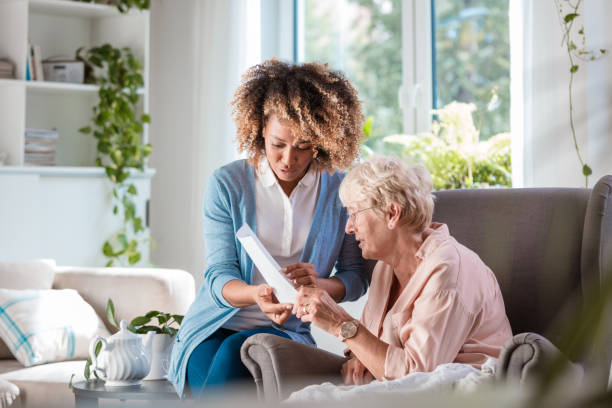 Home nurse taking care of senior woman Female home caregiver supporting senior woman in her house, explaining her documents. recover tab stock pictures, royalty-free photos & images