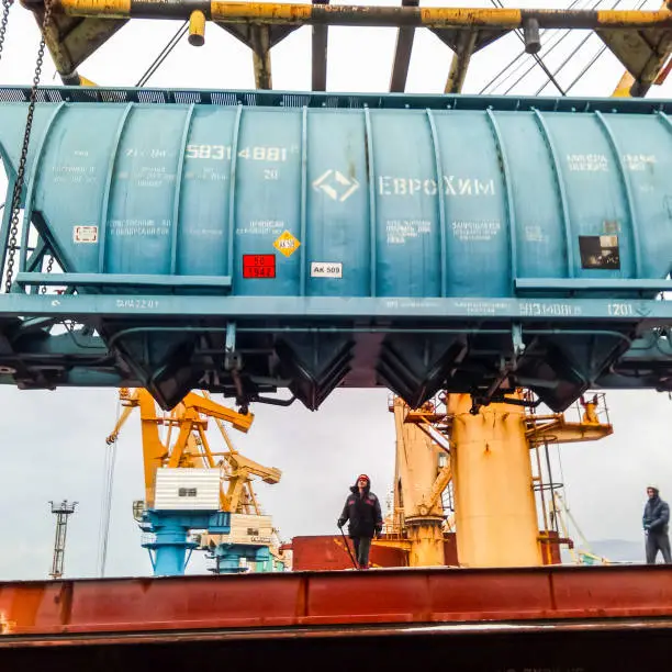 Photo of Moving freight railway car in the port by a port crane. Cargo lifting operations. Industrial port.