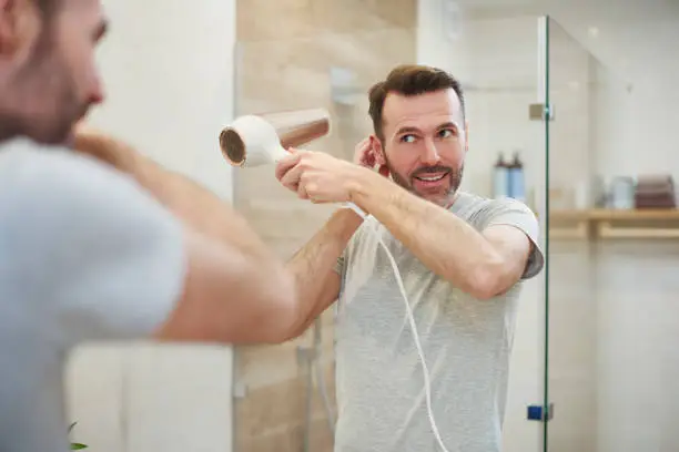 Smiling man using hairdryer in bathroom