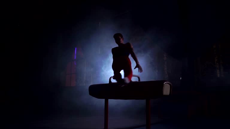 male gymnast athlete performs handstand and spin on Pommel horse on a dark background and smoke in slow motion. Olympic programme