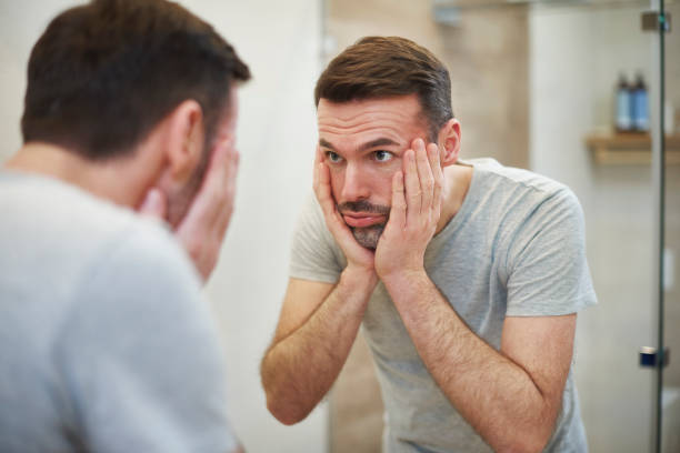 Worried man looking in the mirror in bathroom Worried man looking in the mirror in bathroom low self esteem stock pictures, royalty-free photos & images