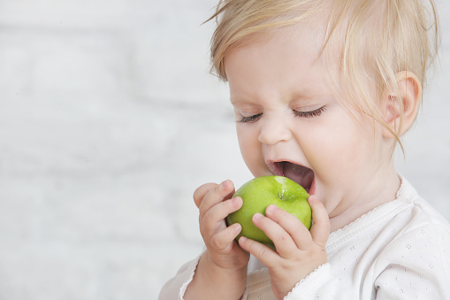 Baby eat an organic green apple - fresh apple as perfect healthy finger food for little ones