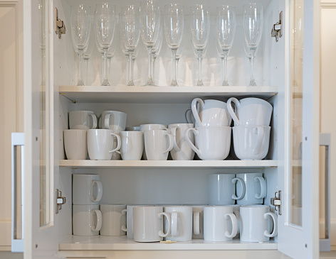 Cupboard full of white mugs and champagne glasses