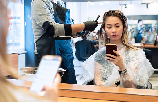 Woman on mobile phone when having hair coloring process in a hair salon