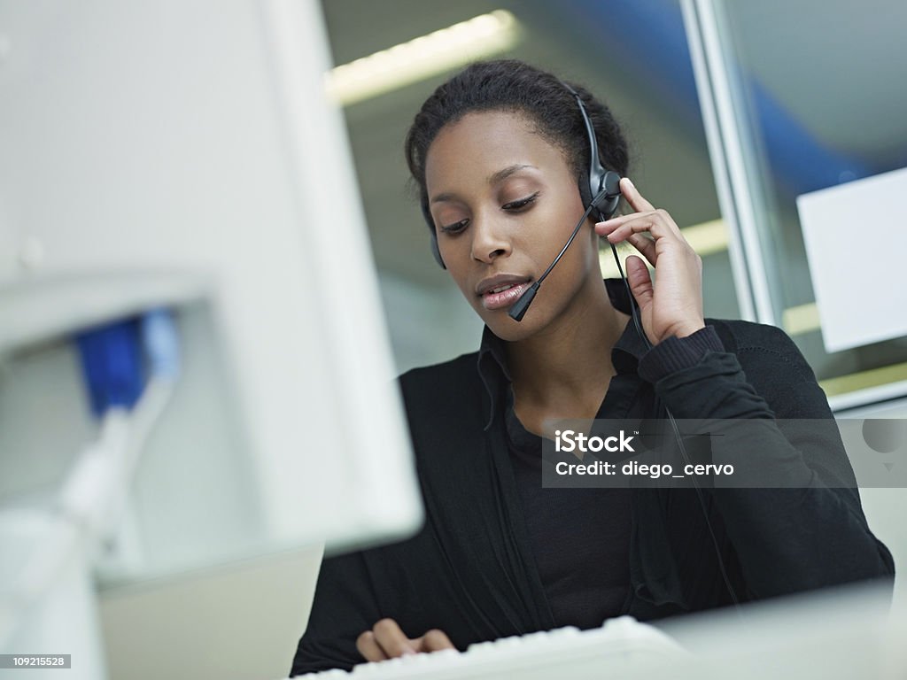 woman working in call center female african american customer service representative with headset typing on computer. Horizontal shape, front view, waist up Serious Stock Photo