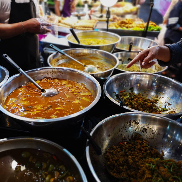 A Thai woman customer points to a delicious Thai curry soup that she would like to order from the seller at a fast food Thai street food market stall in Thailand. This would normally be  served on a bed of fresh steamed white rice.