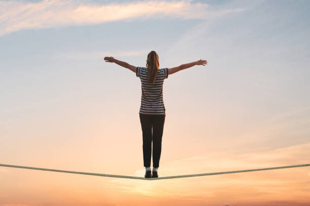 uma garota fica na corda e levanta as mãos contra o pôr do sol. - tightrope balance walking rope - fotografias e filmes do acervo