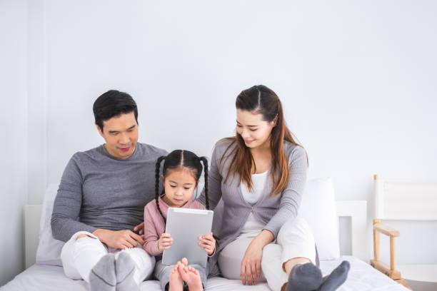 Asian family mother, father and daughter with happy feeling using tablet play game on white bed Asian family mother, father and daughter with happy feeling using tablet play game on white bed lifestyles teaching little girls child stock pictures, royalty-free photos & images