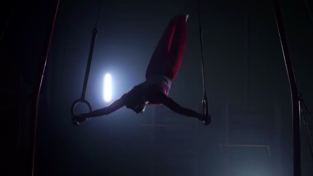 Gymnast on a dark background stands on his hands using rings in the air. Performs rotation in the Olympic program